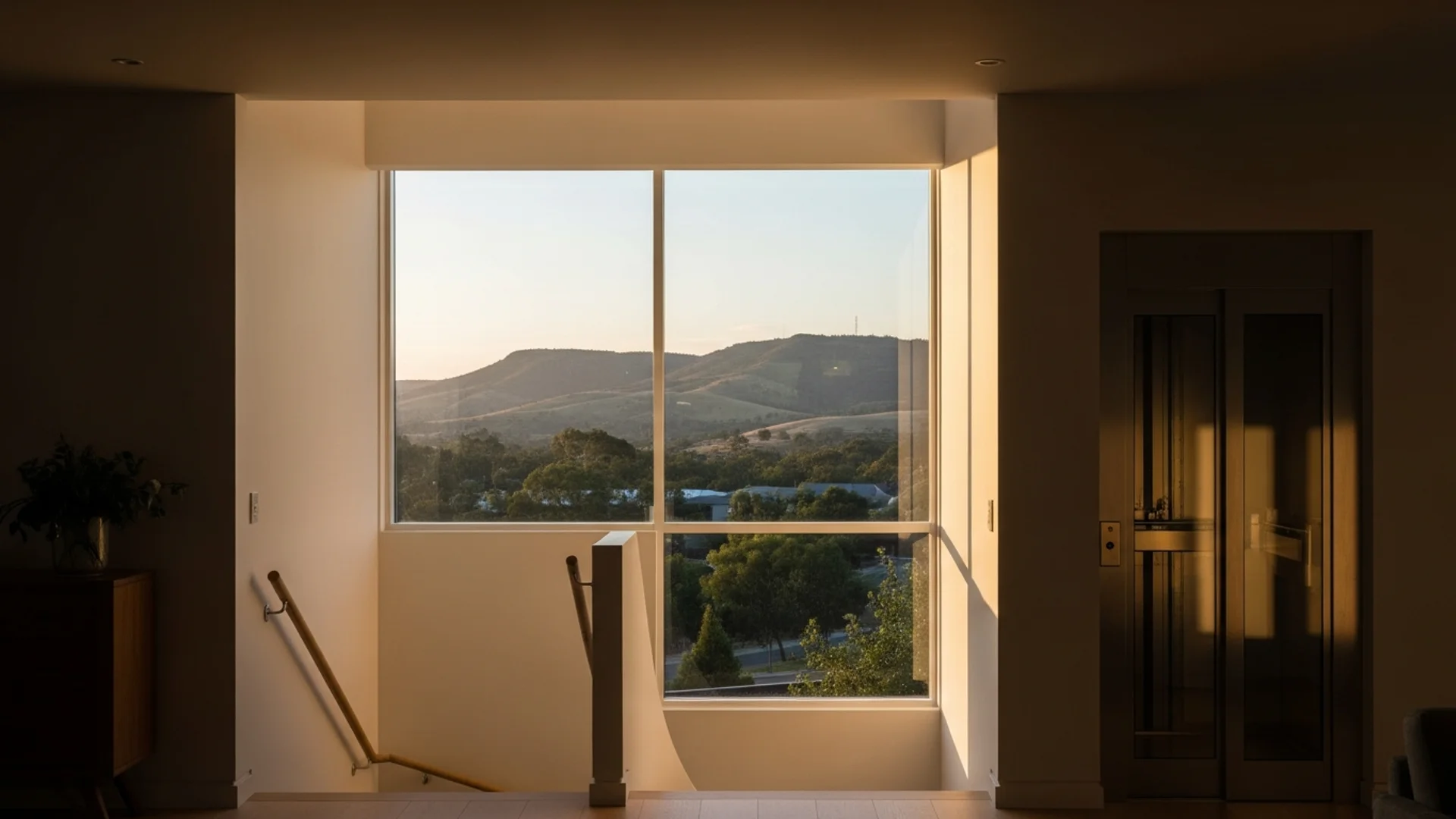 Contemporary Adelaide home interior with a residential lift installed beside an internal staircase, Adelaide Hills visible through large windows